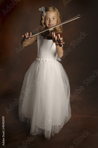 Foto: A girl in white lacy dress playing violin. A girl in white lacy dress playing violin.