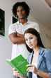 A lady reading a book while her african american boyfriend standing beside her folding his arms.