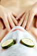 Top angle view of a woman doing facial mask with sliced cucumbers covering her eyes.
