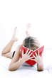A woman lying forward on the bed with her legs up covering her face with a book.