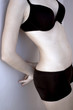 Shoulder down shot of a woman in black bra and panties leaning against the wall.