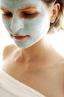 Close-up of a woman in towel with blue facial mask on her face.