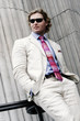 A guy in business suit and sunglasses keeping his hands in the pockets.