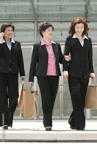 Photo: Three ladies in formal wear walking together carrying paper bags. Three ladies in formal wear walking together carrying paper bags.