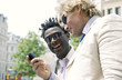 A guy in white suit and sunglasses showing his african american friend the messages in his handphone.