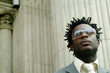 a man in business suit with sunglass looking at the building opposite.