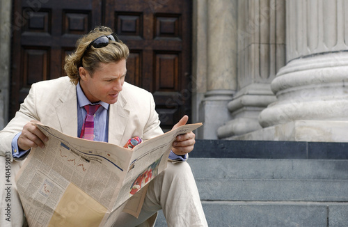 Photo: a man with a sunglass on his head sitting on the stairs reading newspaper. a man with a sunglass on his head sitting on the stairs reading newspaper.