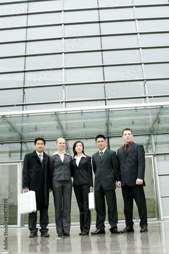 Photo: A group of business people standing in front of their office building. A group of business people standing in front of their office building.