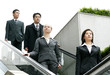 Photo: A group of business people coming down from an escalator. A group of business people coming down from an escalator.