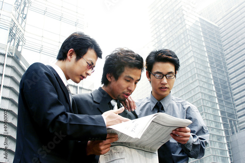 Photo: Three businessmen sharing a newspaper. Three businessmen sharing a newspaper.