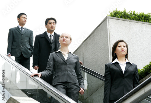 Photo: A group of business people coming down from an escalator. A group of business people coming down from an escalator.