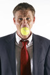 Businessman's mouth being stuffed with a tennis ball. 