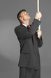 Man in business suit pulling a rope hanging from the top. 