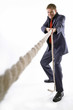 Man in business suit pulling a rope with all his might. 