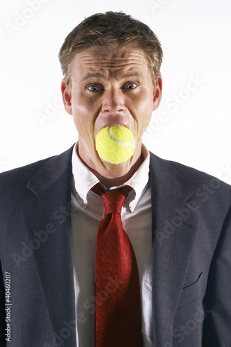Photo: Businessman's mouth being stuffed with a tennis ball. Businessman's mouth being stuffed with a tennis ball.