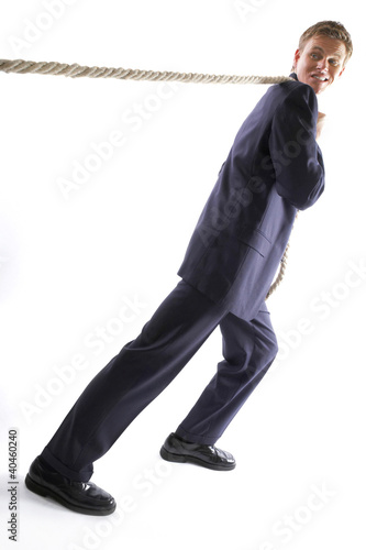 Photo: Man in business suit pulling a rope with all his might. Man in business suit pulling a rope with all his might.