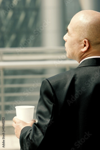 Photo: Back shot of a bald man in business suit holding a cup. Back shot of a bald man in business suit holding a cup.
