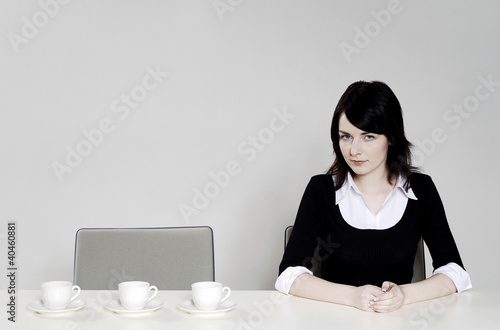 Photo: Businesswoman sitting beside three arranged cups. Businesswoman sitting beside three arranged cups.