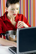 Woman using laptop while cooking.