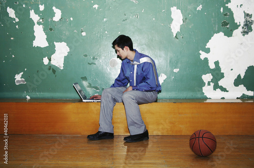 Photo: Businessman using laptop in a basketball court. Businessman using laptop in a basketball court.