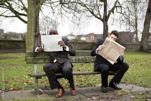 Photo: Two businessmen reading newspaper on the bench. Two businessmen reading newspaper on the bench.