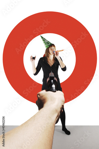 Photo: Hand aiming a pistol at a businesswoman with party hat. Hand aiming a pistol at a businesswoman with party hat.