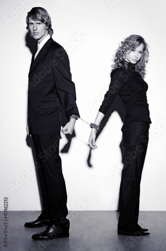 Photo: Businessman and businesswoman being cuffed together. Businessman and businesswoman being cuffed together.