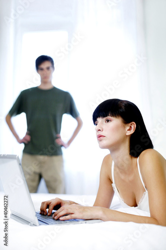Photo: Man watching his wife using laptop. Man watching his wife using laptop.
