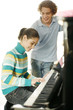 Boy watching his sister playing piano.