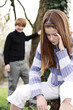 A boy looking at a sad looking girl who is sitting alone.