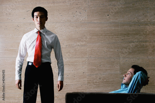 Photo: One businessman standing while the other one relaxing on the couch. One businessman standing while the other one relaxing on the couch.