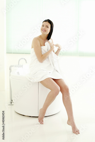 Photo: Woman sitting on bathtub ledge drying her hair with a towel Woman sitting on bathtub ledge drying her hair with a towel