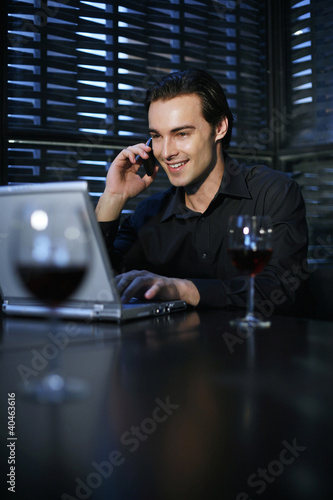 Foto: Man talking on the mobile phone while using laptop in the restaurant Man talking on the mobile phone while using laptop in the restaurant