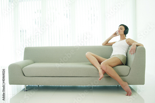 Photo: Woman sitting on the couch listening to music on the headphones Woman sitting on the couch listening to music on the headphones