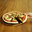 Hand taking slice of freshly cooked pizza with mushroom, anchovies and basil topping