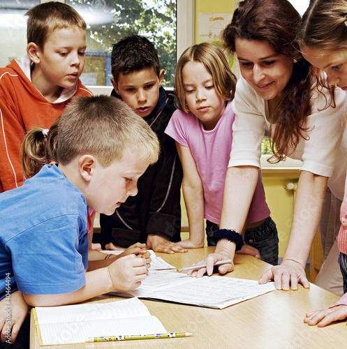 Foto: Female teacher looking at a book with her students surrounding her Female teacher looking at a book with her students surrounding her