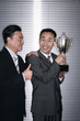 Businessman with a trophy with another businessman congratulating him