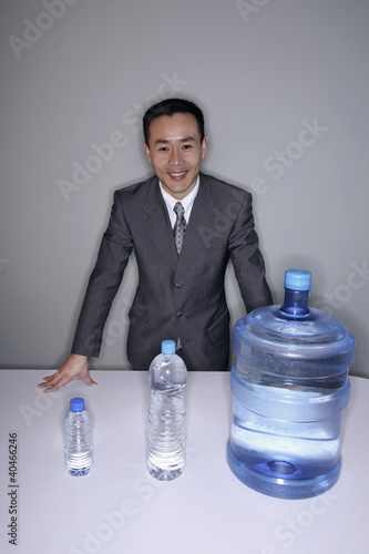 Photo: Businessman smiling at the camera with three water bottles on the table Businessman smiling at the camera with three water bottles on the table
