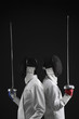 Two men leaning back to back holding fencing foils