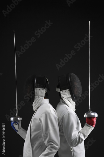 Foto: Two men leaning back to back holding fencing foils Two men leaning back to back holding fencing foils