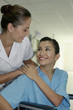 Woman on wheelchair touching nurse's hand while smiling at her