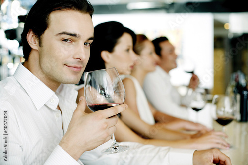 Photo: Man holding a glass of red wine while smiling at the camera Man holding a glass of red wine while smiling at the camera