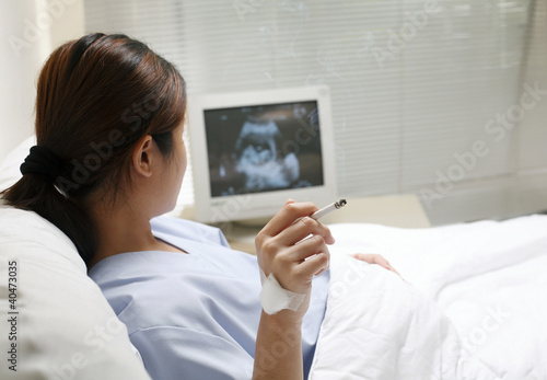 Photo: Pregnant woman lying on the bed smoking Pregnant woman lying on the bed smoking
