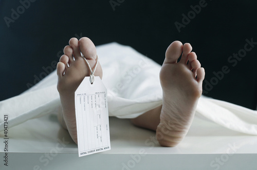 Photo: Toe tag hanging on woman lying on table in morgue Toe tag hanging on woman lying on table in morgue