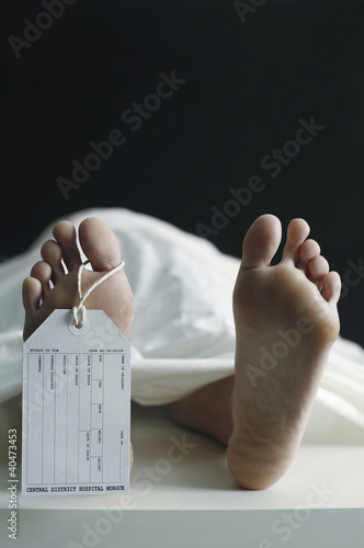 Photo: Toe tag hanging on woman lying on table in morgue Toe tag hanging on woman lying on table in morgue