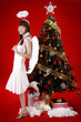 Young woman in angel costume standing beside christmas tree