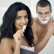 Man shaving his face while his girlfriend is brushing teeth