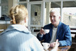 A man lifting a cup of coffee while talking to his wife