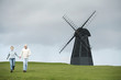 A couple holding hands and walking near a windmill