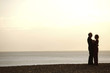 An elderly couple hugging face-to-face on the beach, during sunset